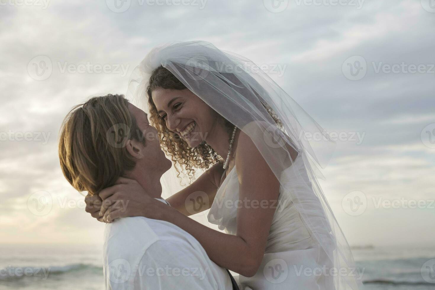 Romantic newlyweds at beach against sky during sunset photo