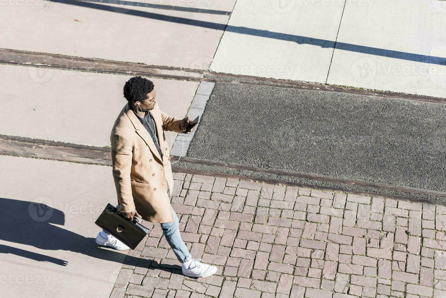 empresario caminando al aire libre con maletín, célula teléfono y auriculares foto