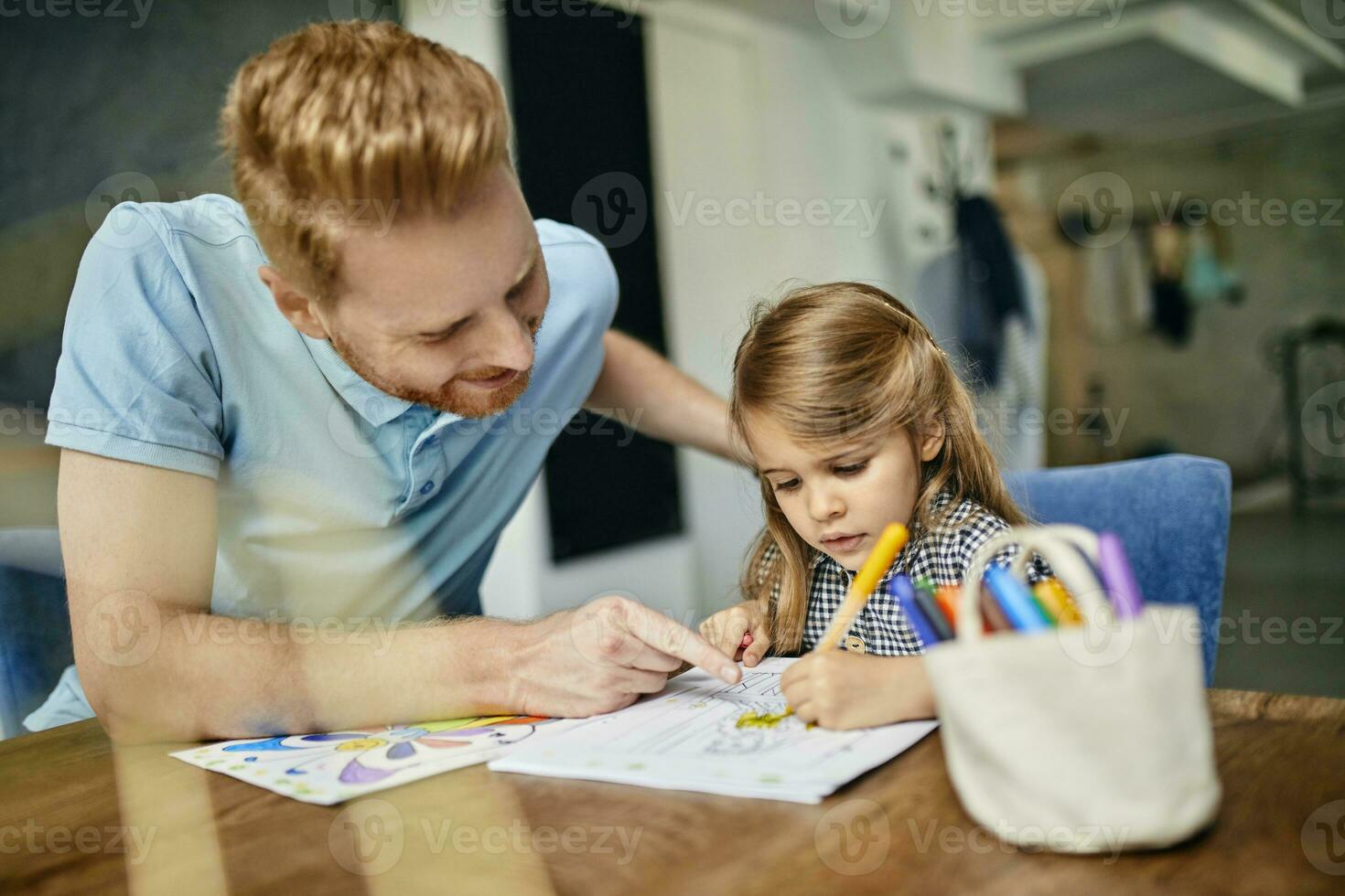 Father and daughter sitting at table, painting colouring book photo