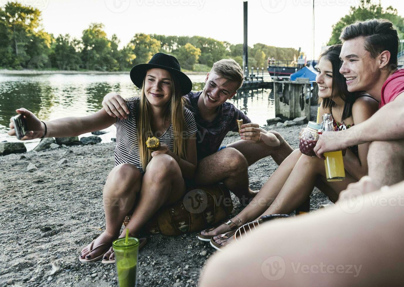 Group of friends sitting together having a barbecue and taking a selfie at the riverside photo