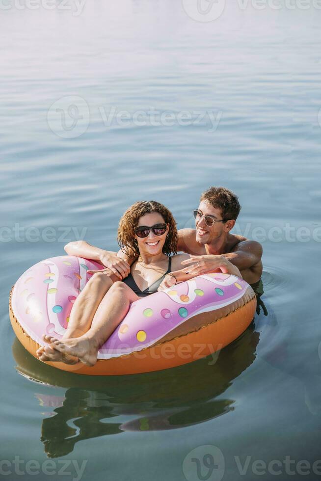 contento joven Pareja baños en el mar en inflable flotador en rosquilla forma foto