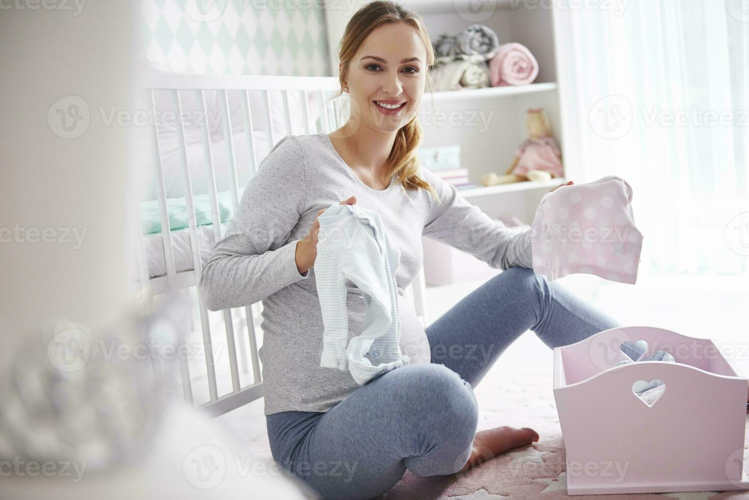 Pregnant woman with baby clothes in baby room photo