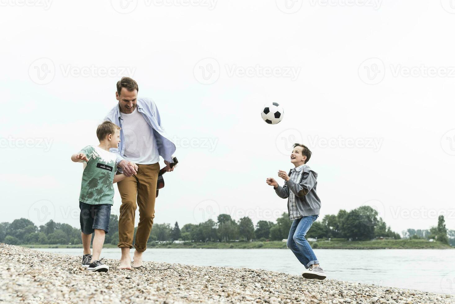 Happy father with two sons and football walking at the riverside photo