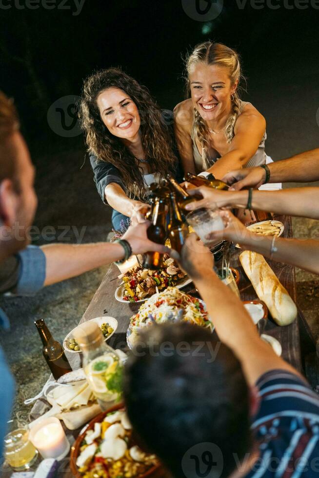 Happy friends toasting with beer bottles during an outdoor dinner photo