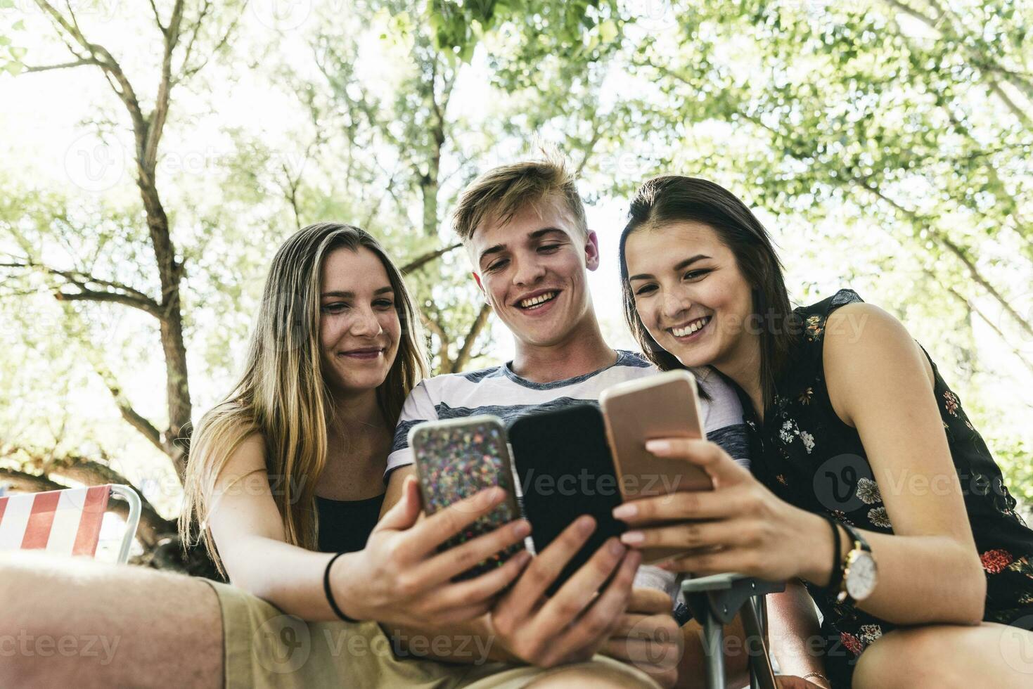 Tres contento amigos mirando a célula Los telefonos al aire libre foto