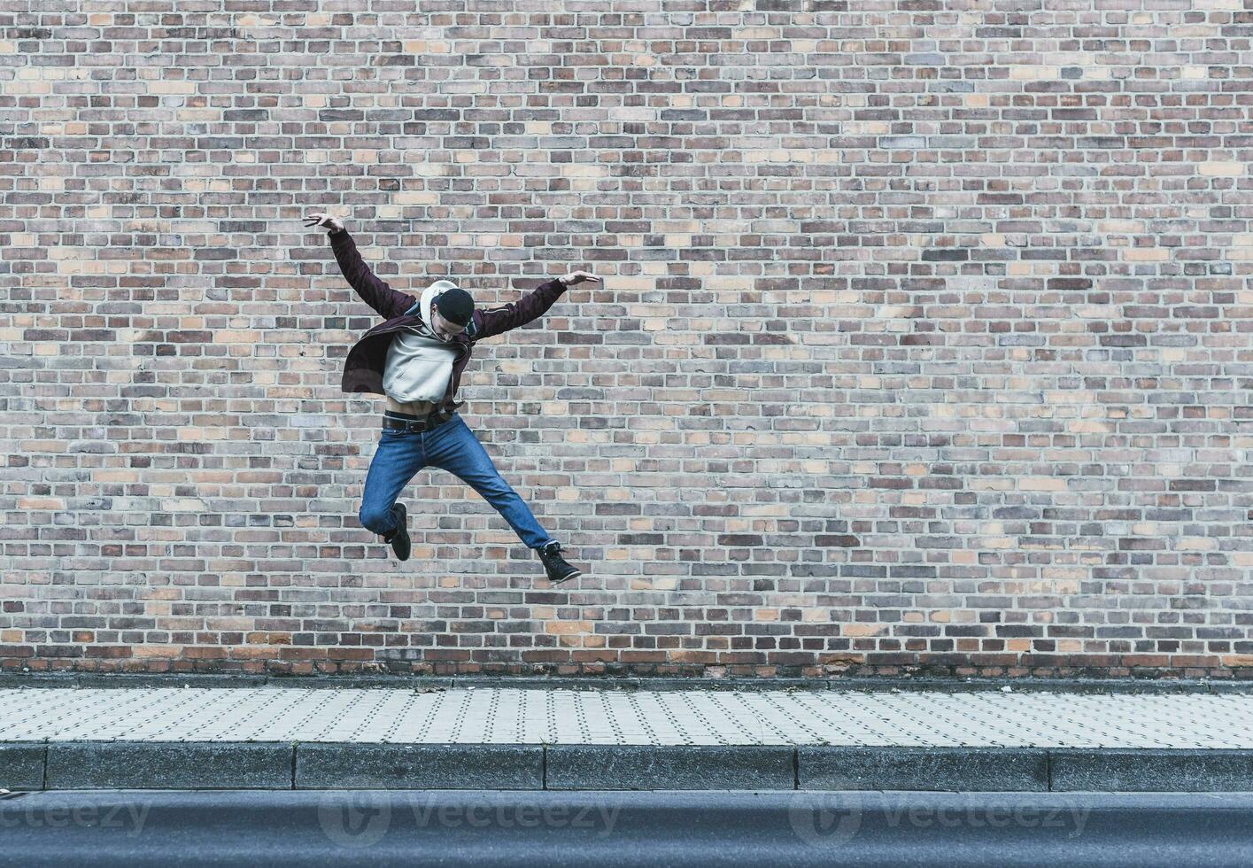 Young man jumping in front of brick wall photo