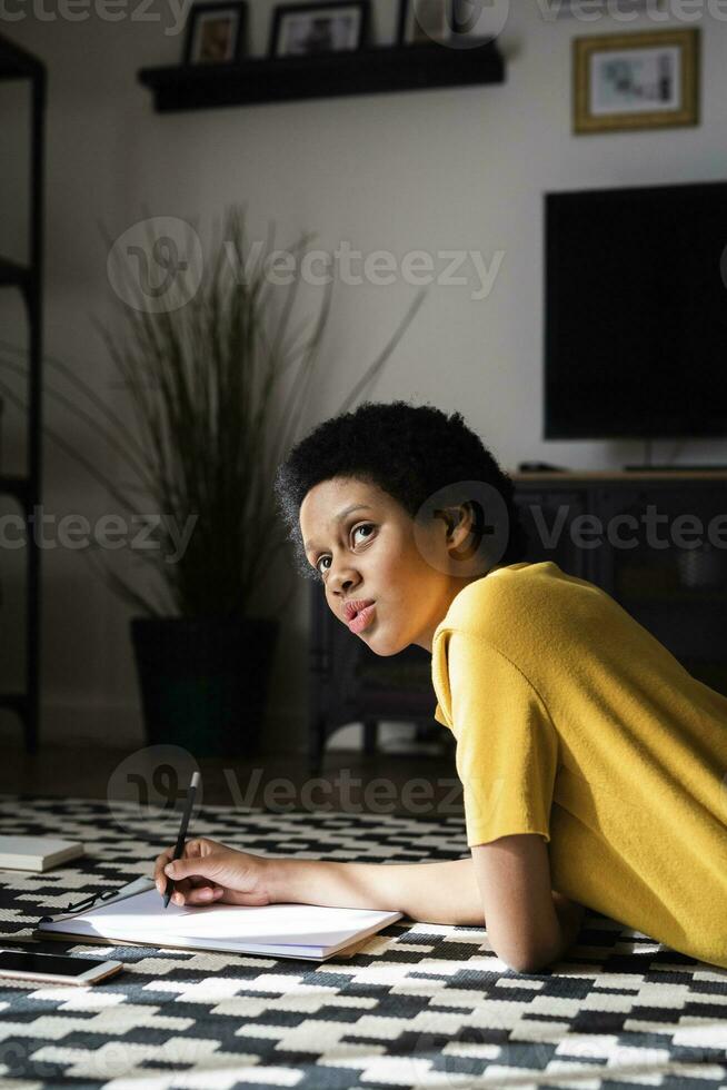 Young woman lying on the floor at home taking notes photo