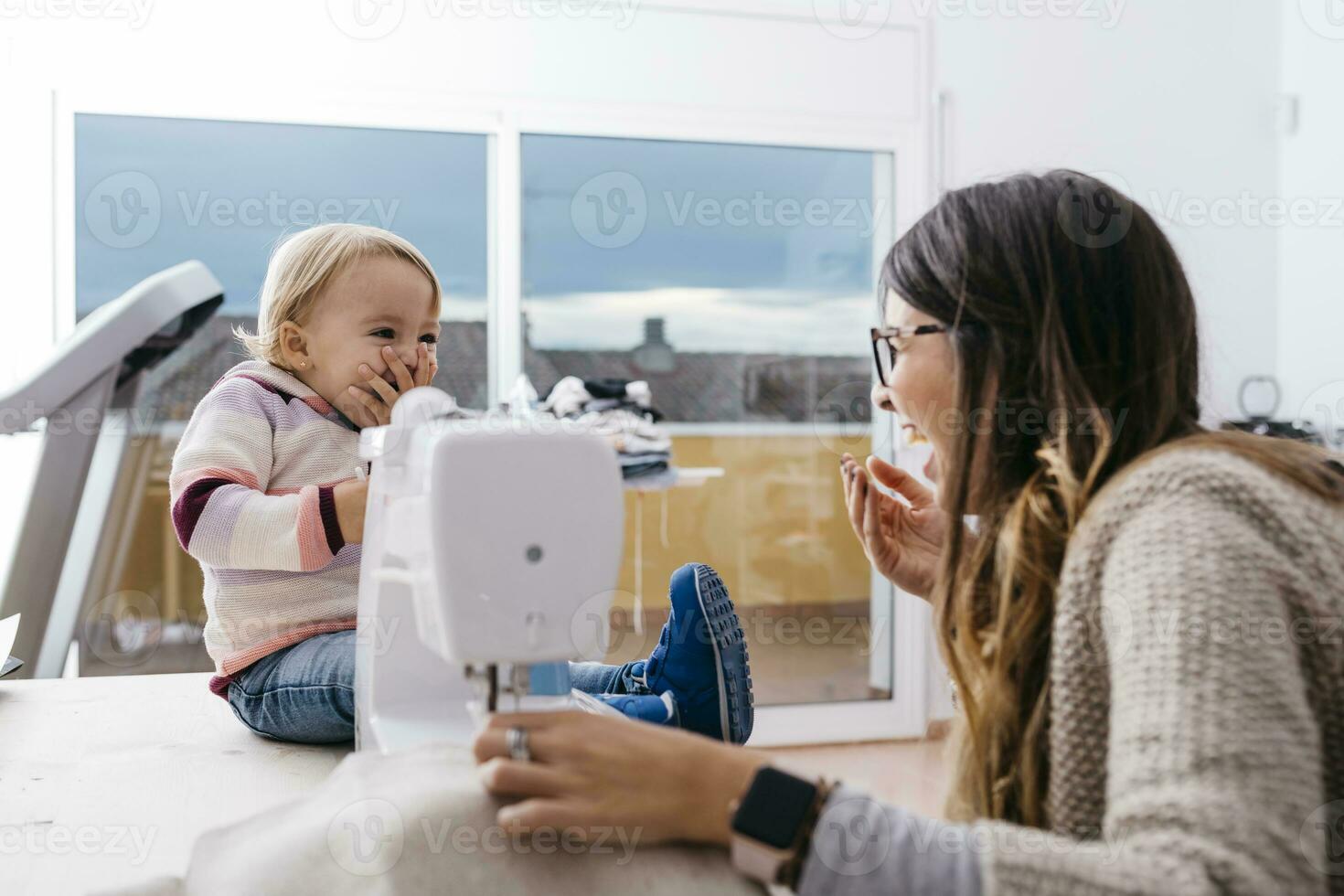 Happy mother with little daughter at home using sewing machine photo