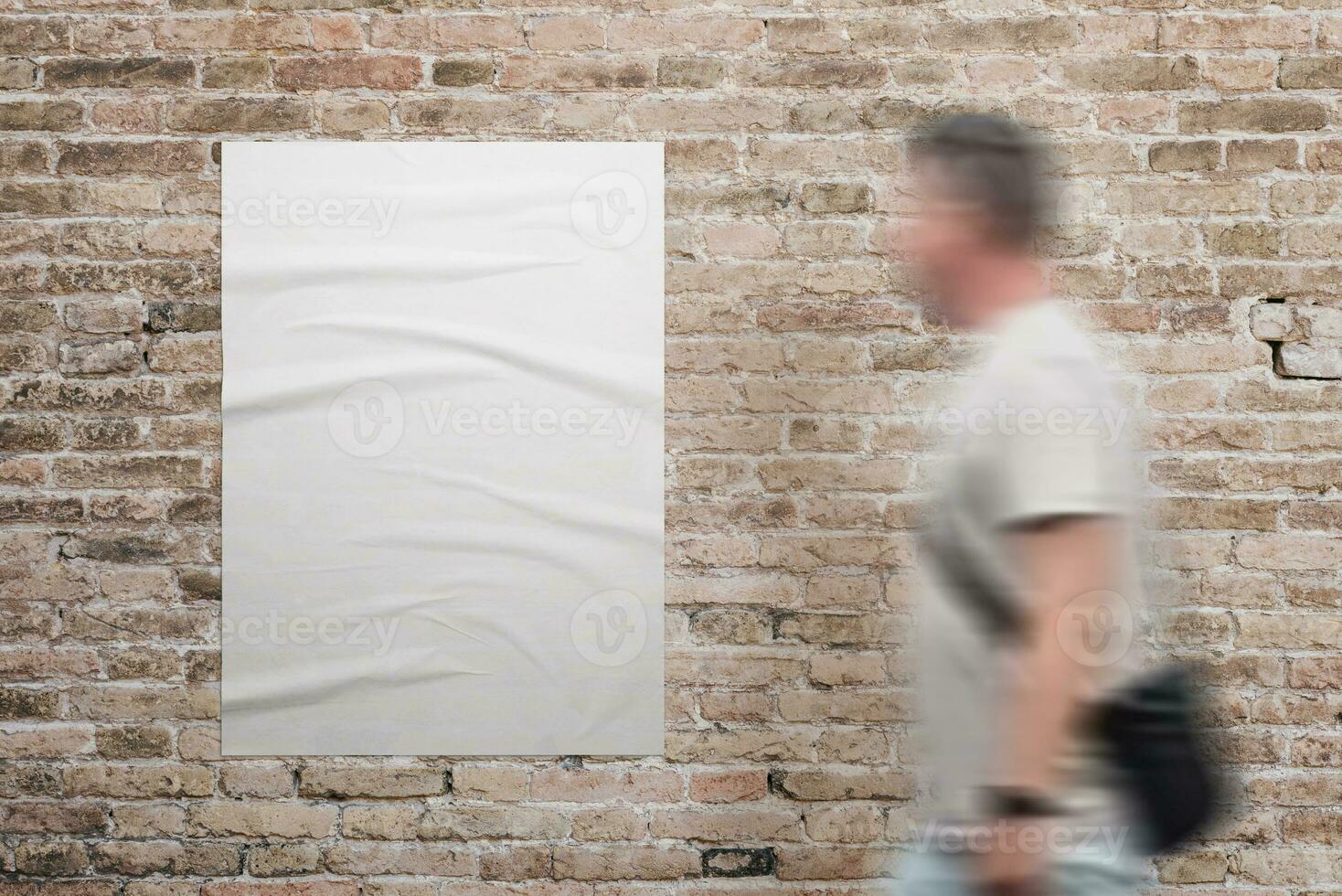 Wrinkled, blank A3 poster in white, adhered to a brick wall. A man walks beside. Ad or marketing campaign design promotion photo