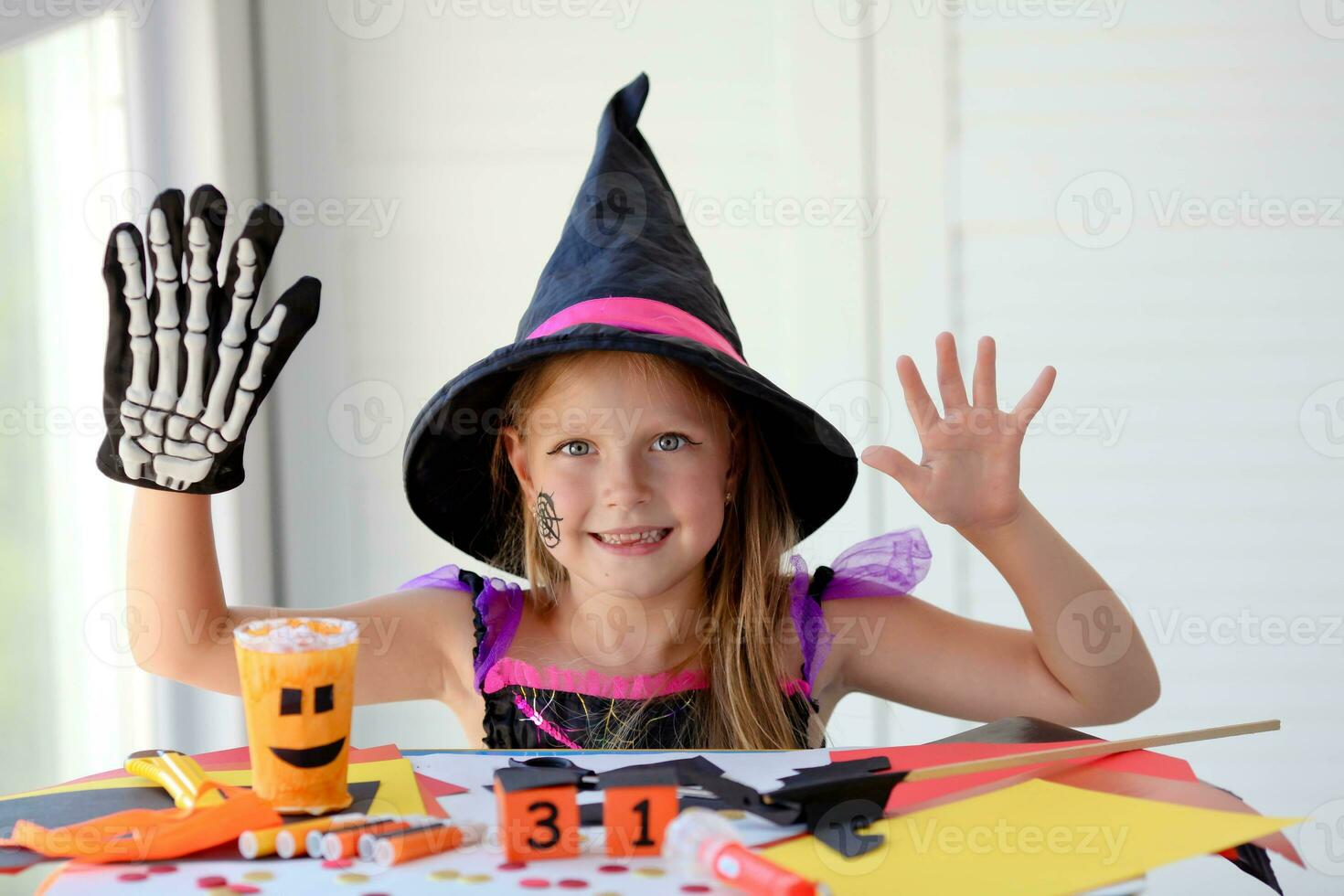 A little girl in a witch costume looks at the camera and laughs, holding a skeleton glove. photo