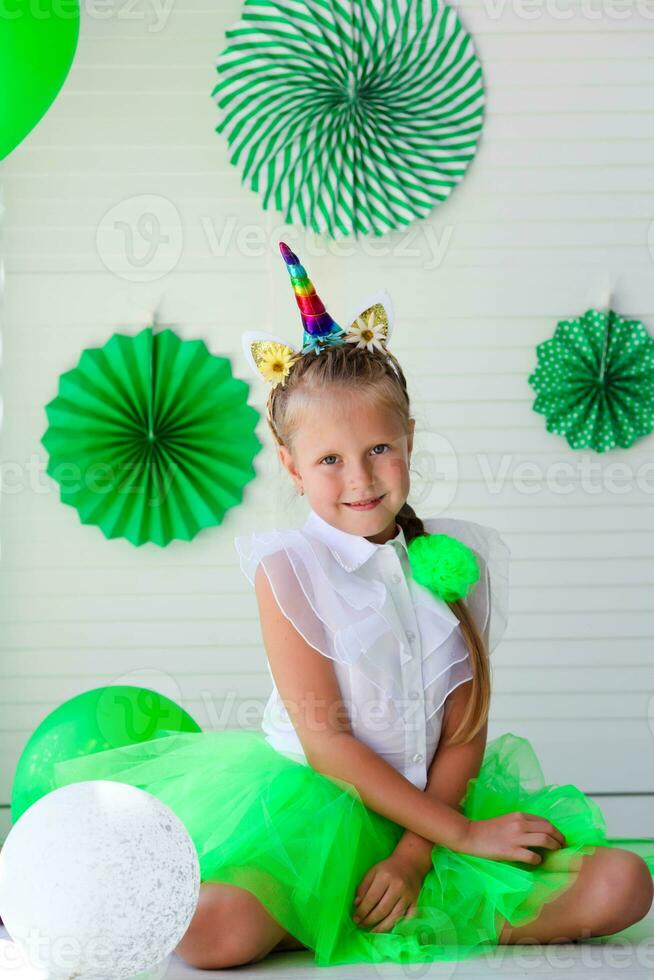 A little girl with a unicorn hoop on her head against a background of green photo decoration. Birthday for children. St. Patrick is Day Celebration