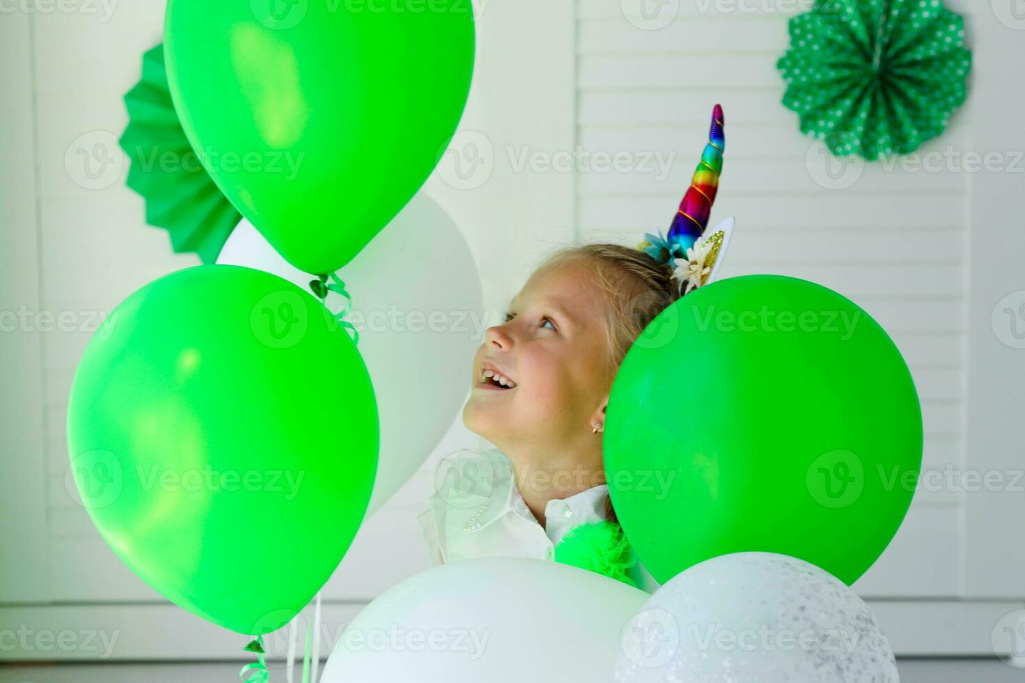 Little girl with a unicorn hoop on her head against the background of green balloons. Birthday for children. photo