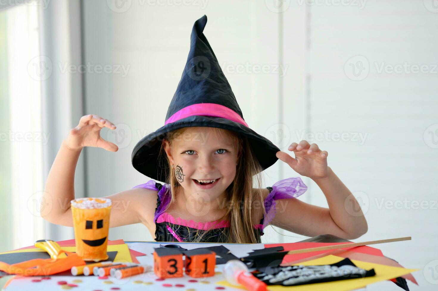 A little girl in a witch costume looks at the camera and scares. photo