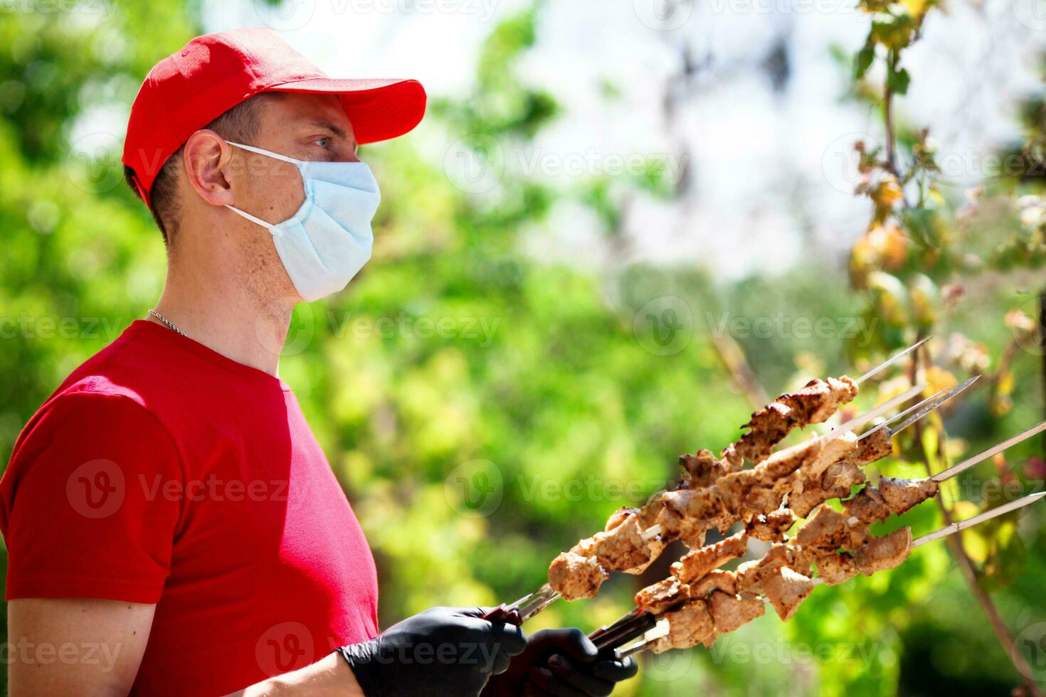 A man in a medical mask and rubber gloves holds skewers with barbecue. Safe cooking. Courier. Food delivery during quarantine due to the coronavirus pandemic. photo