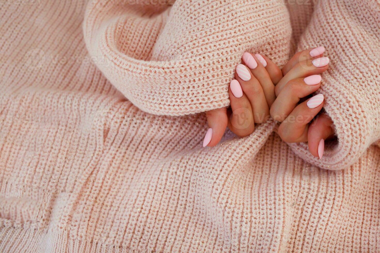 Female hands with beautiful oval-shaped nails, matte pink manicure close-up on a pink knitted sweater background. Shellac. photo