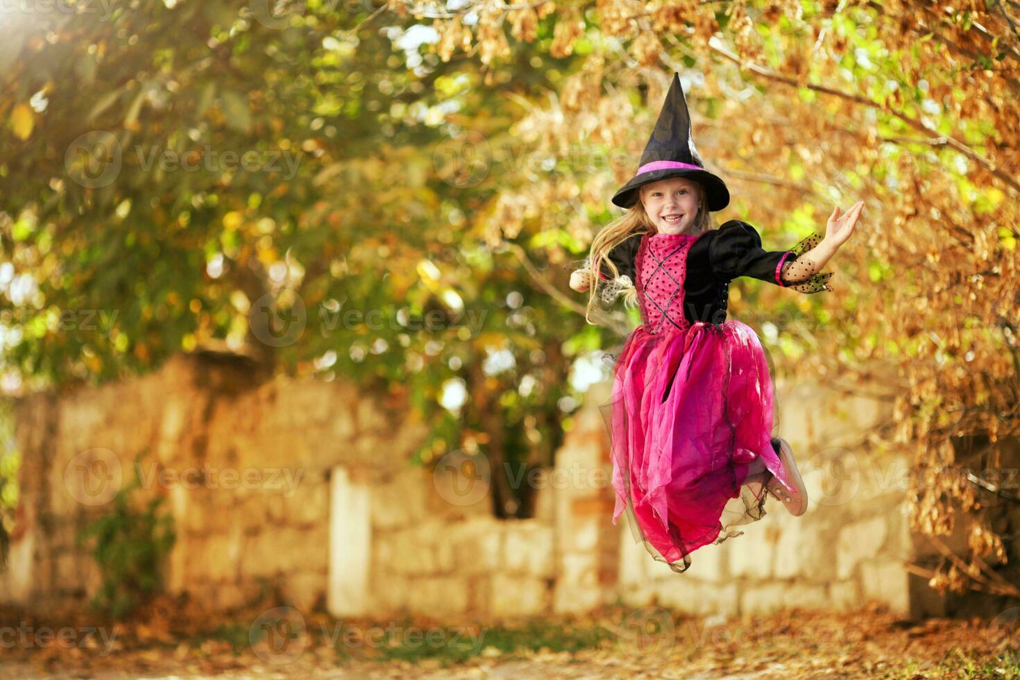 A little girl in a witch costume is jumping on the street. Halloween holiday. photo