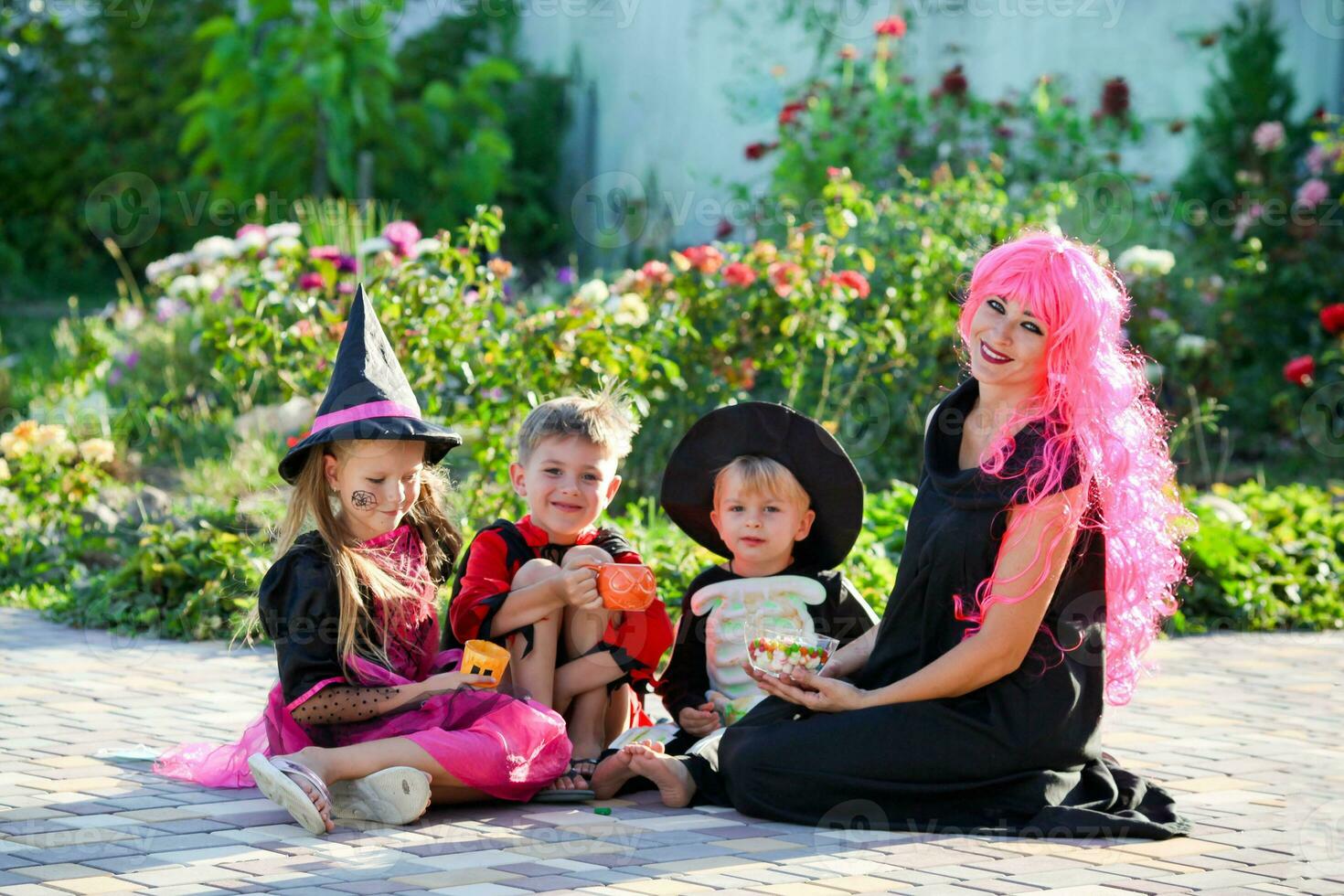 Young kids trick or treating during Halloween . Children and a woman are sitting on the road in halloween costumes. photo