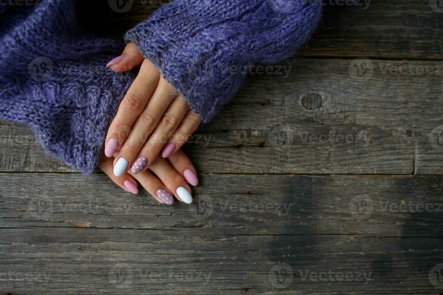 Women is hands with a beautiful manicure, in a knitted sweater on a wooden background in. Autumn trend, polish beige and white polka dots on nails with gel polish, shellac. photo