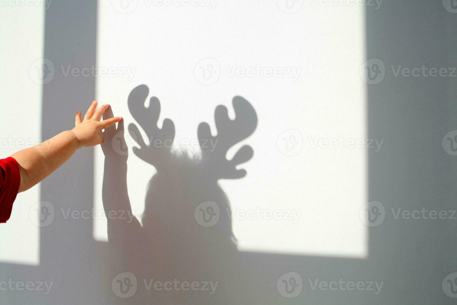 Child touches his shadow on the wall with his hand. Shadow of a kid with deer antlers, christmas concept. photo