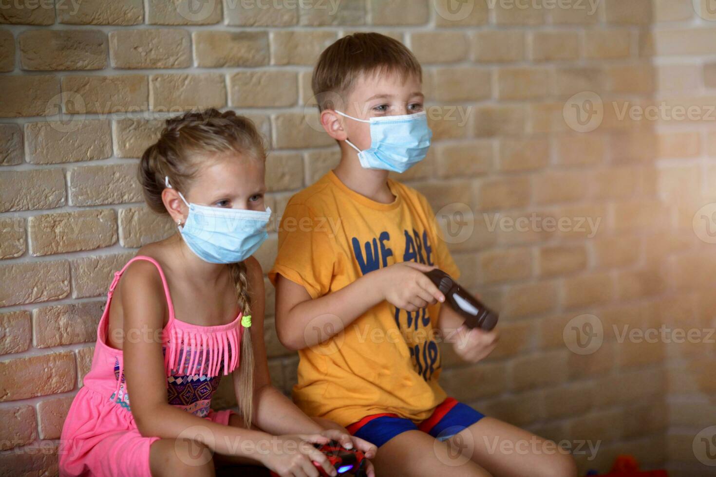 Little girl and boy play medical mask game console while sitting on sofa at home. photo