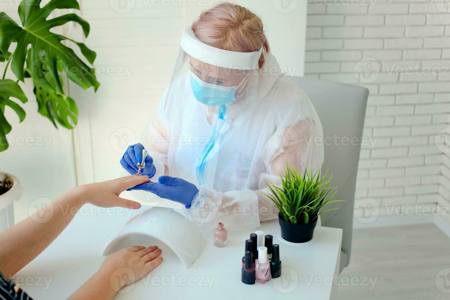 Manicurist in are wearing PPE paints nails in a beauty salon. Professional procedure. The existence of small businesses in isolation from COVID-19. photo