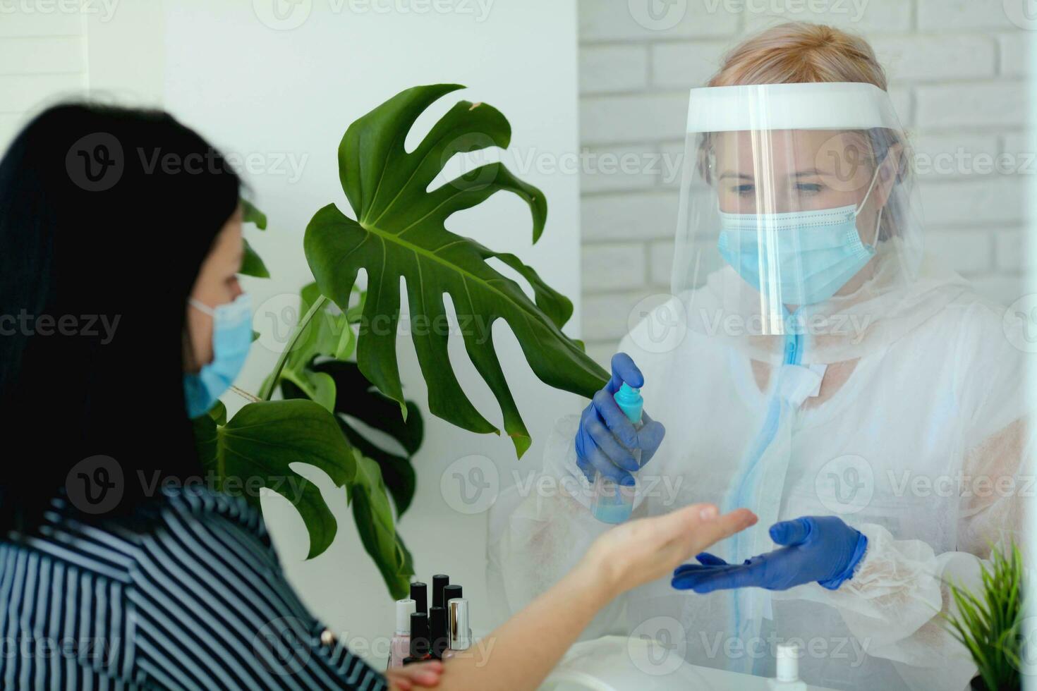 A manicurist in a protective mask and clothes in a beauty salon treats his hands with an antispecialist. Professional procedure. photo