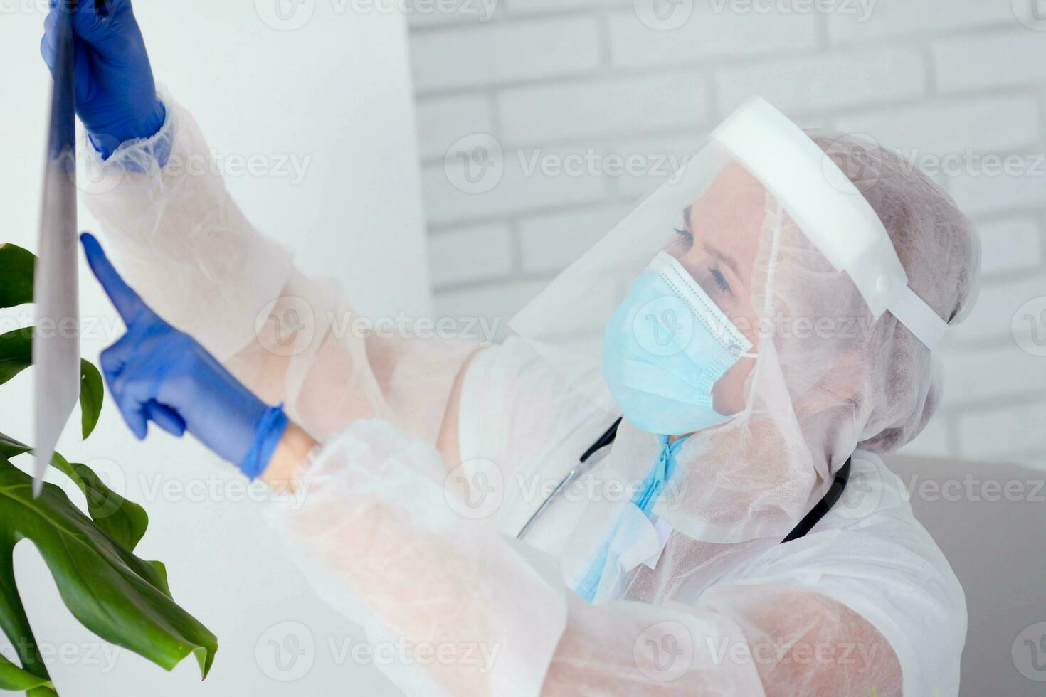 The doctor in are wearing PPE looks at the x-ray picture. Woman doctor  protective suit works during a pandemic COVID -19. photo