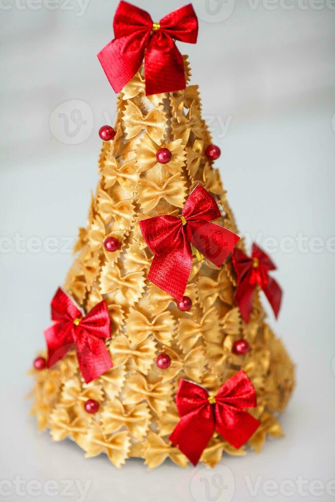 niños es artesanía. Navidad árbol hecho de pasta, pintado oro y decorado con un rojo arco. foto