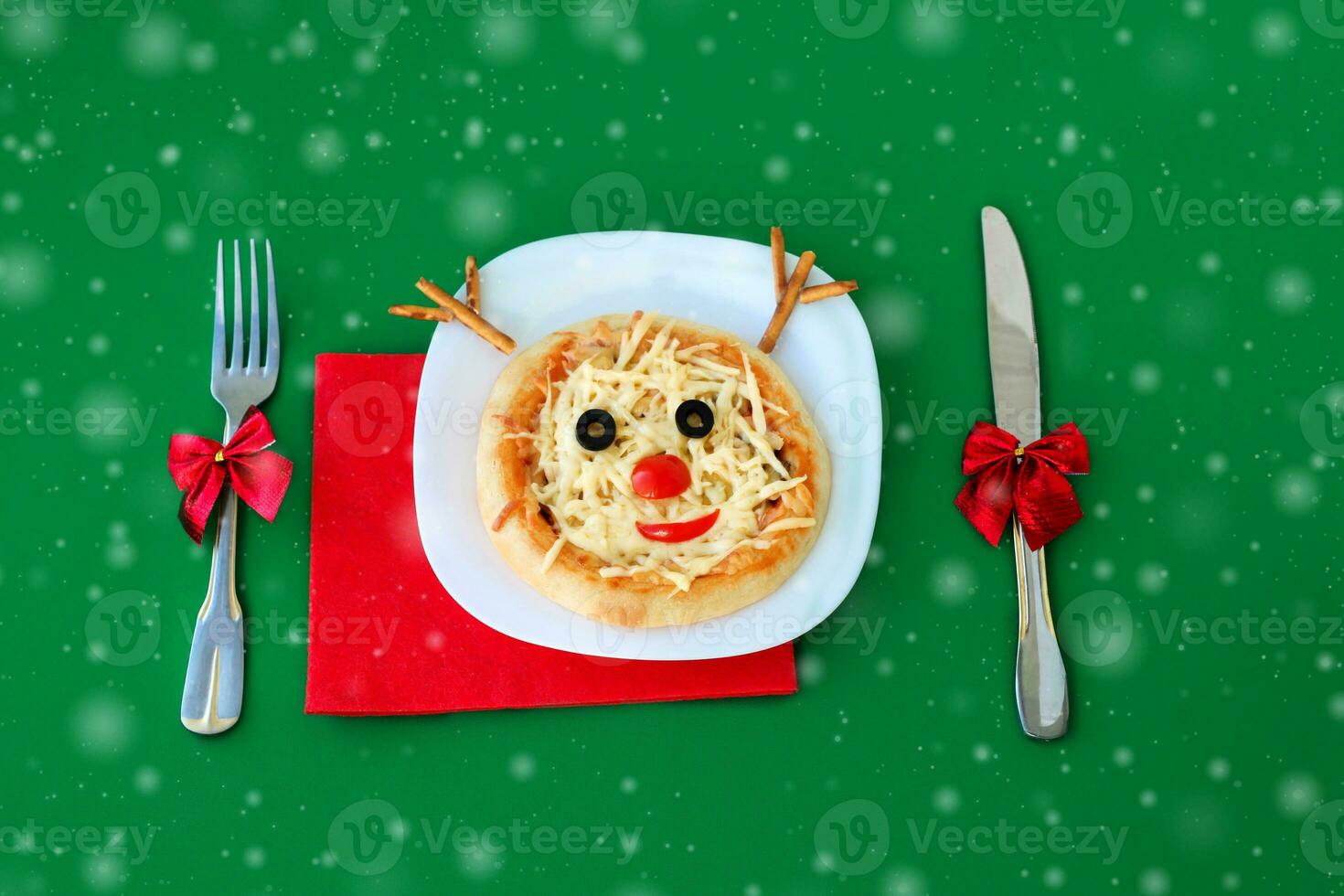 Christmas pizza in a shape of reindeer and cutlery  on a green background. photo