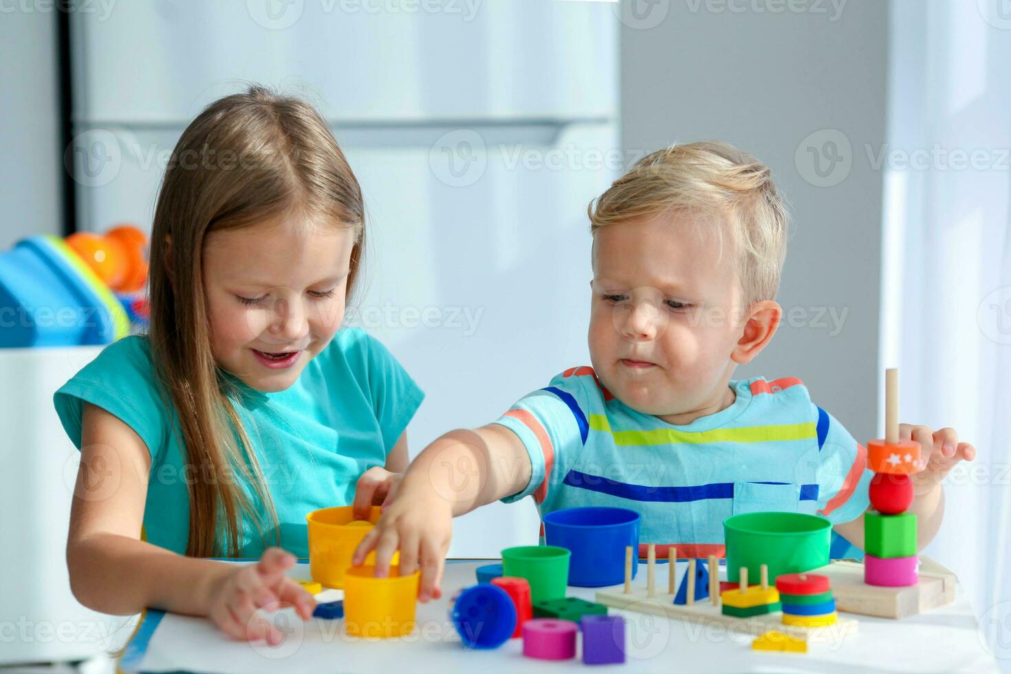 Sister helps little brother to assemble the pyramid. Educational logical toys for children. Montessori games for child development. photo