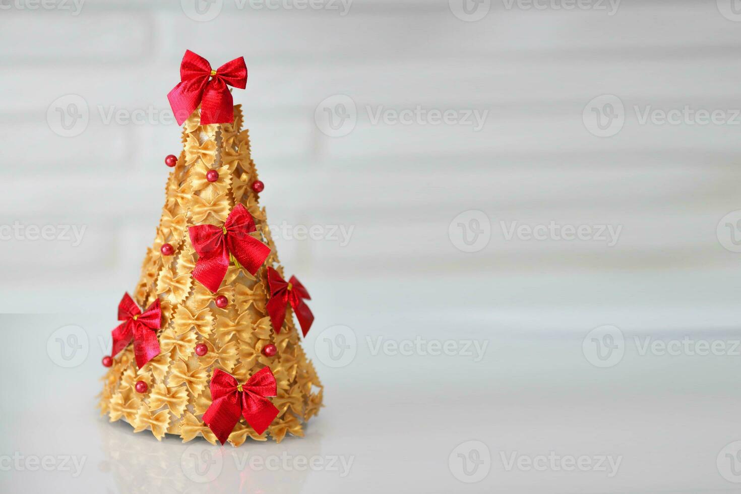 Children is craft. Christmas tree made of pasta, painted gold and decorated with a red bow.  Handmade, DIY. photo