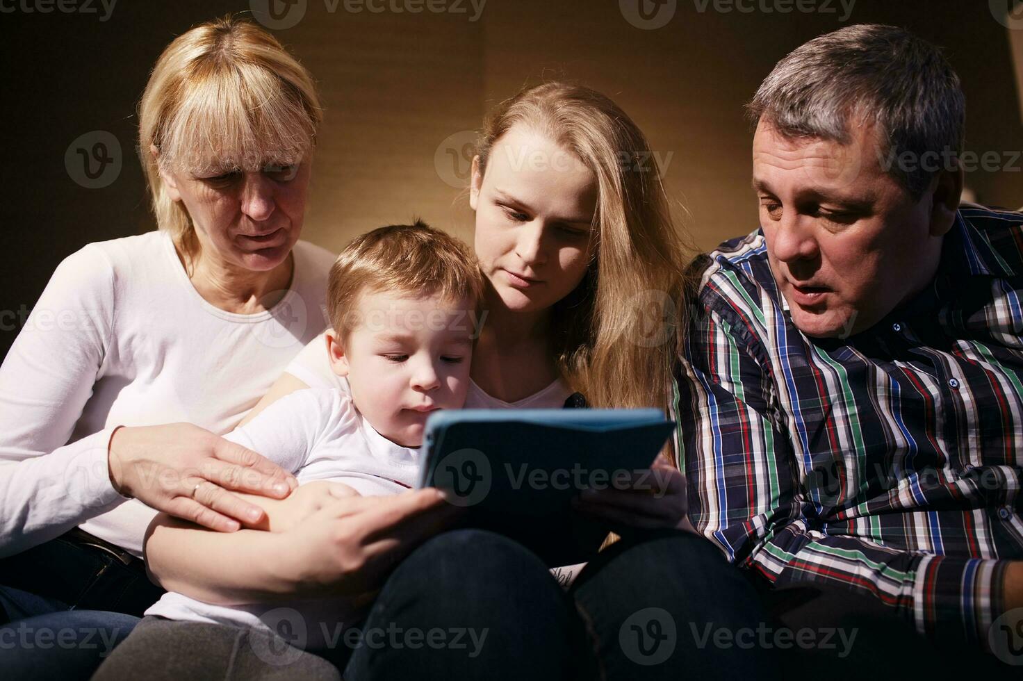 Family watching boy playing game on touchpad photo