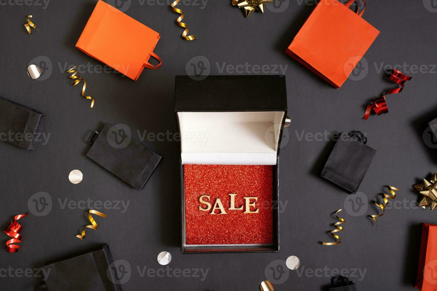 Black friday sale concept. Sale text in black gift box and shopping bags with festive decorations on black background flat lay, top view. photo