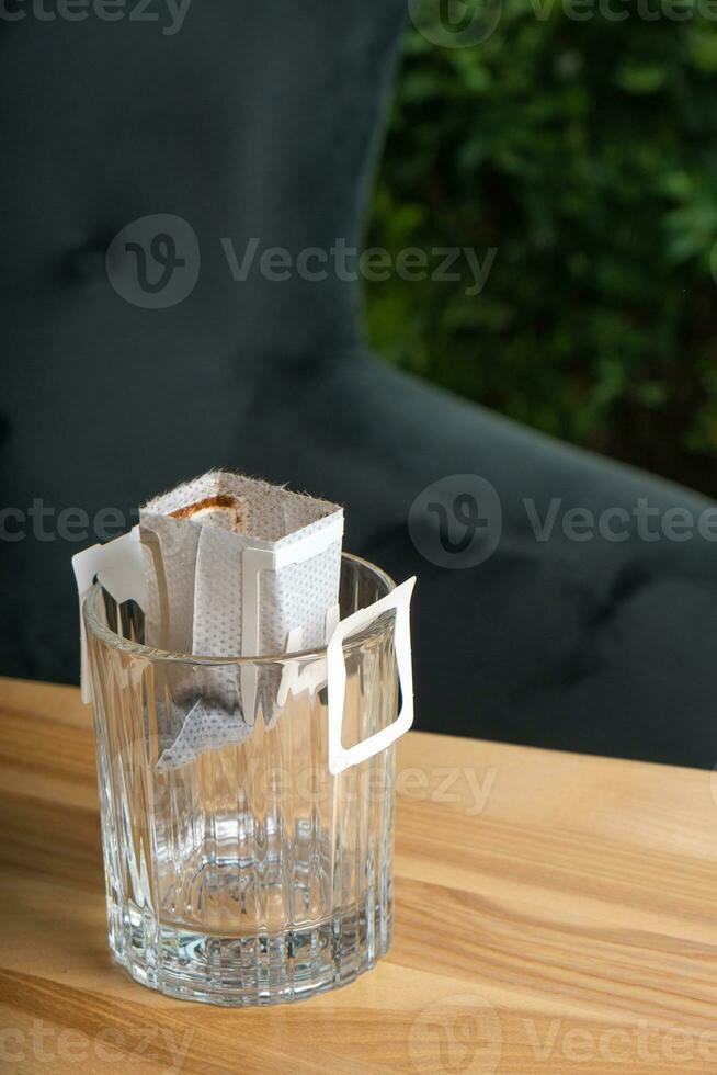 Glass cup with drip coffee bag on wooden table. Trends in making coffee at home. photo