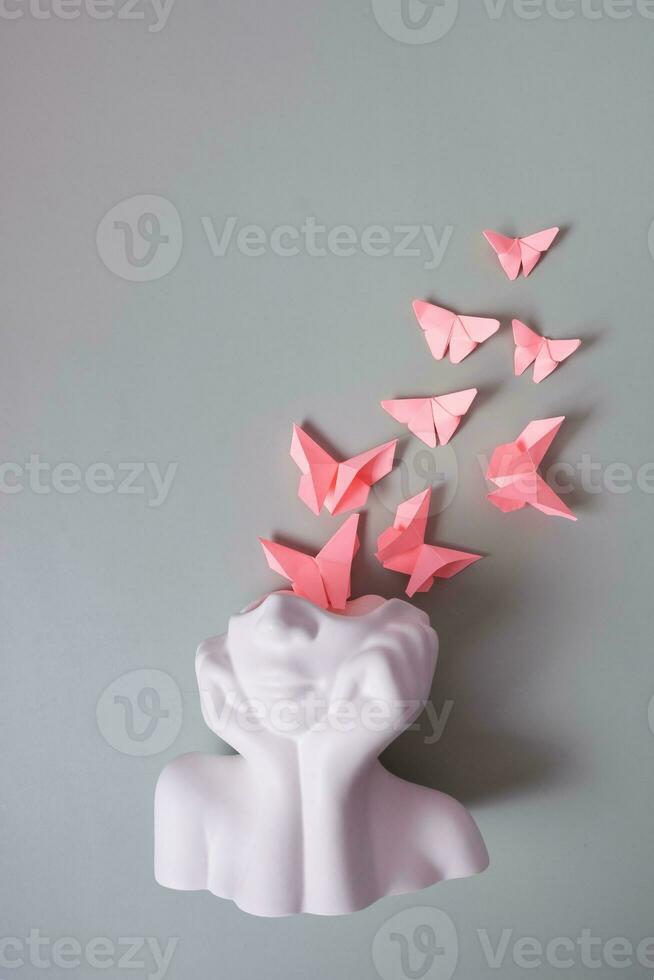 A figurine of a head with pink butterflies on grey background. Mental health concept photo