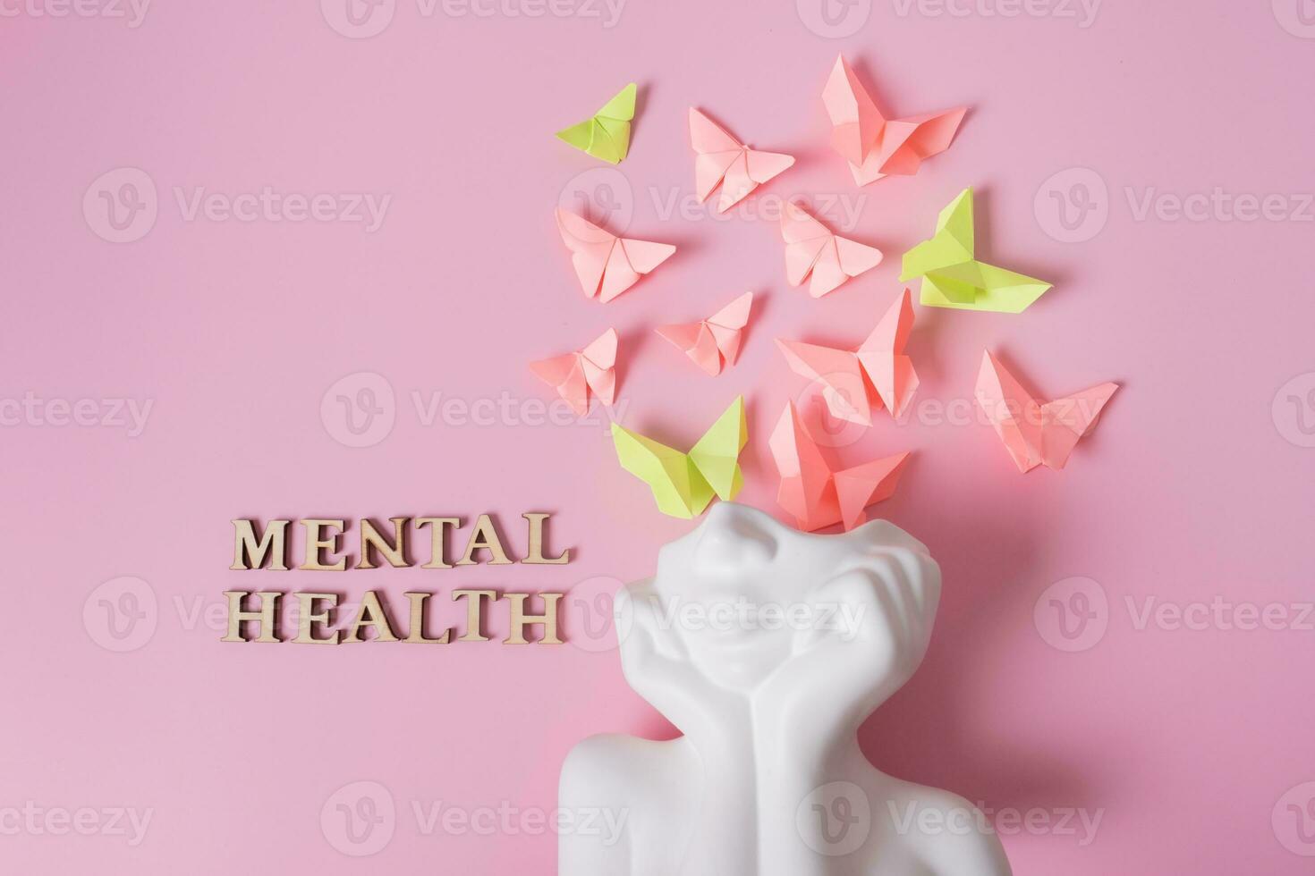 A figurine of a head with butterflies on a pink background. Mental health concept photo