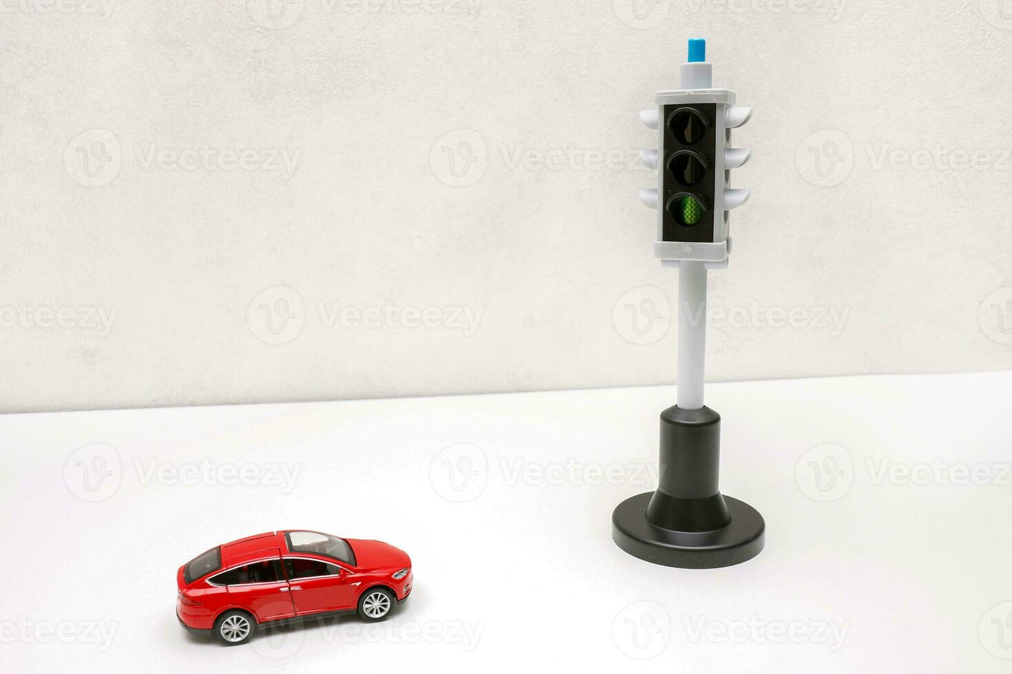 a red toy car stands in front of a traffic light with a green signal photo