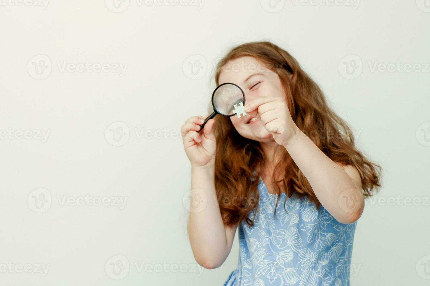 little cute girl examines a puzzle element through a magnifying glass photo