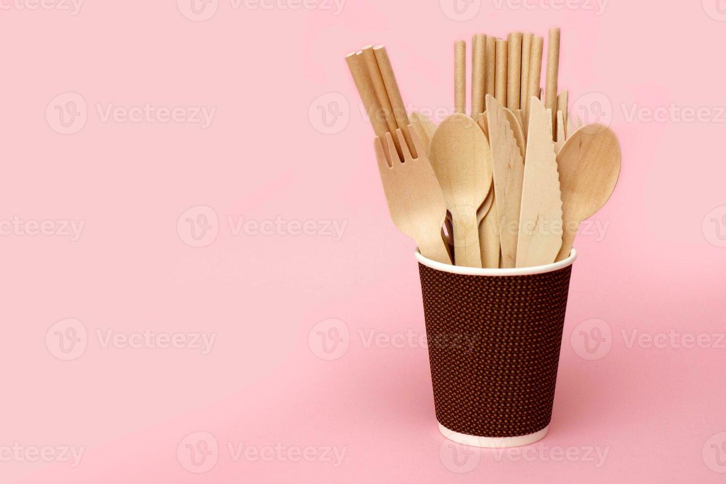 disposable bamboo cutlery in a paper cup on a pink background with copy space photo