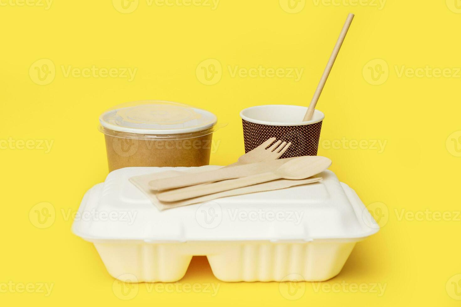 recycled disposable tableware set, soup container, glass with a straw, lunchbox, knife, fork, spoon on a yellow background photo