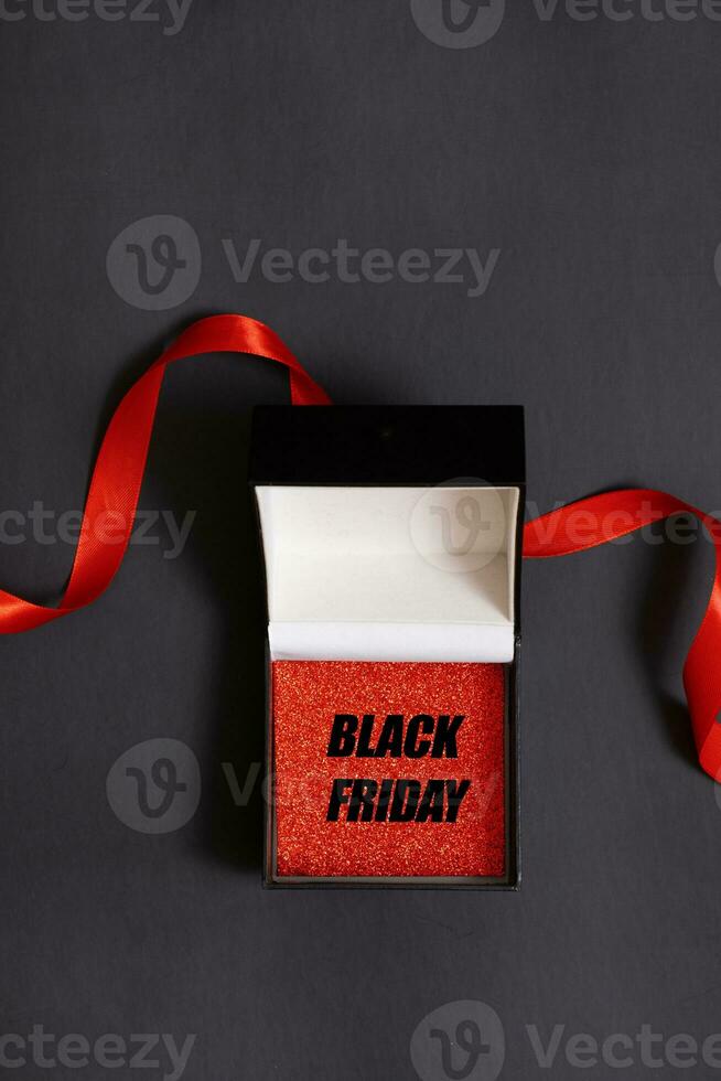 Black friday text in black gift box and red ribbon on black background flat lay, top view. Minimalistic black friday concept. photo