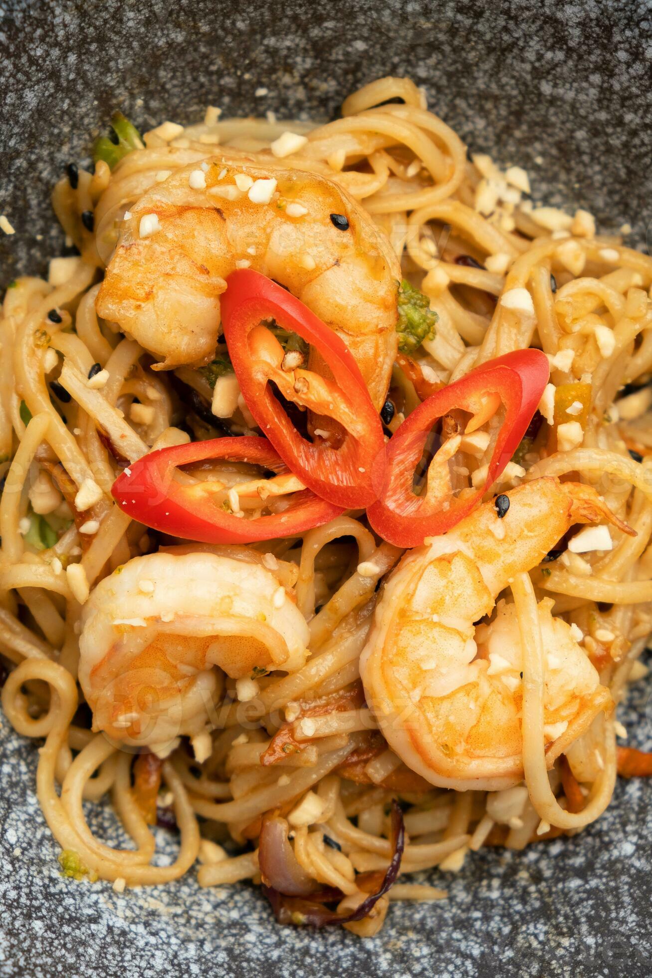 Udon noodles with shrimp and fried vegetables in a bowl close up