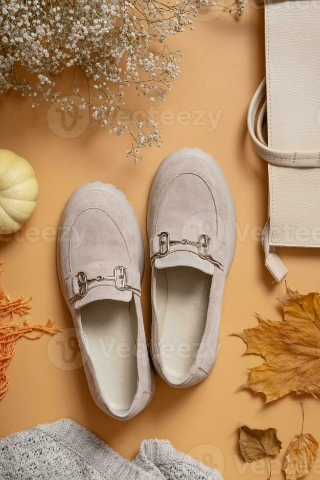 Female suede shoes and bag with autumn leaves and pumpkin on orange background top view, flat lay photo