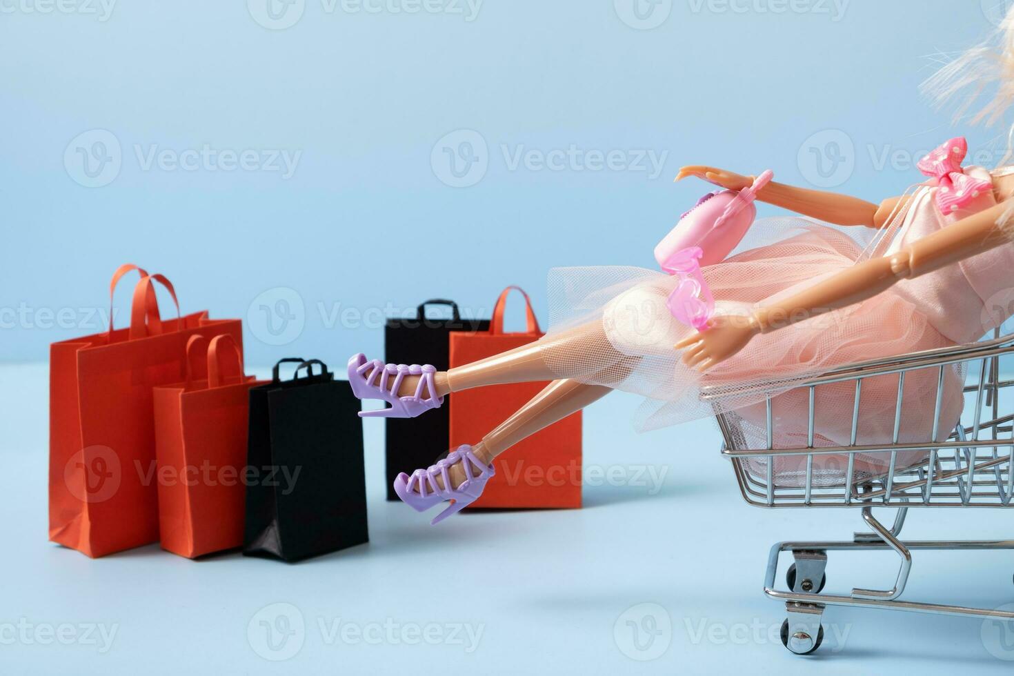 Doll in supermarket basket with shopping bag. Sale concept photo