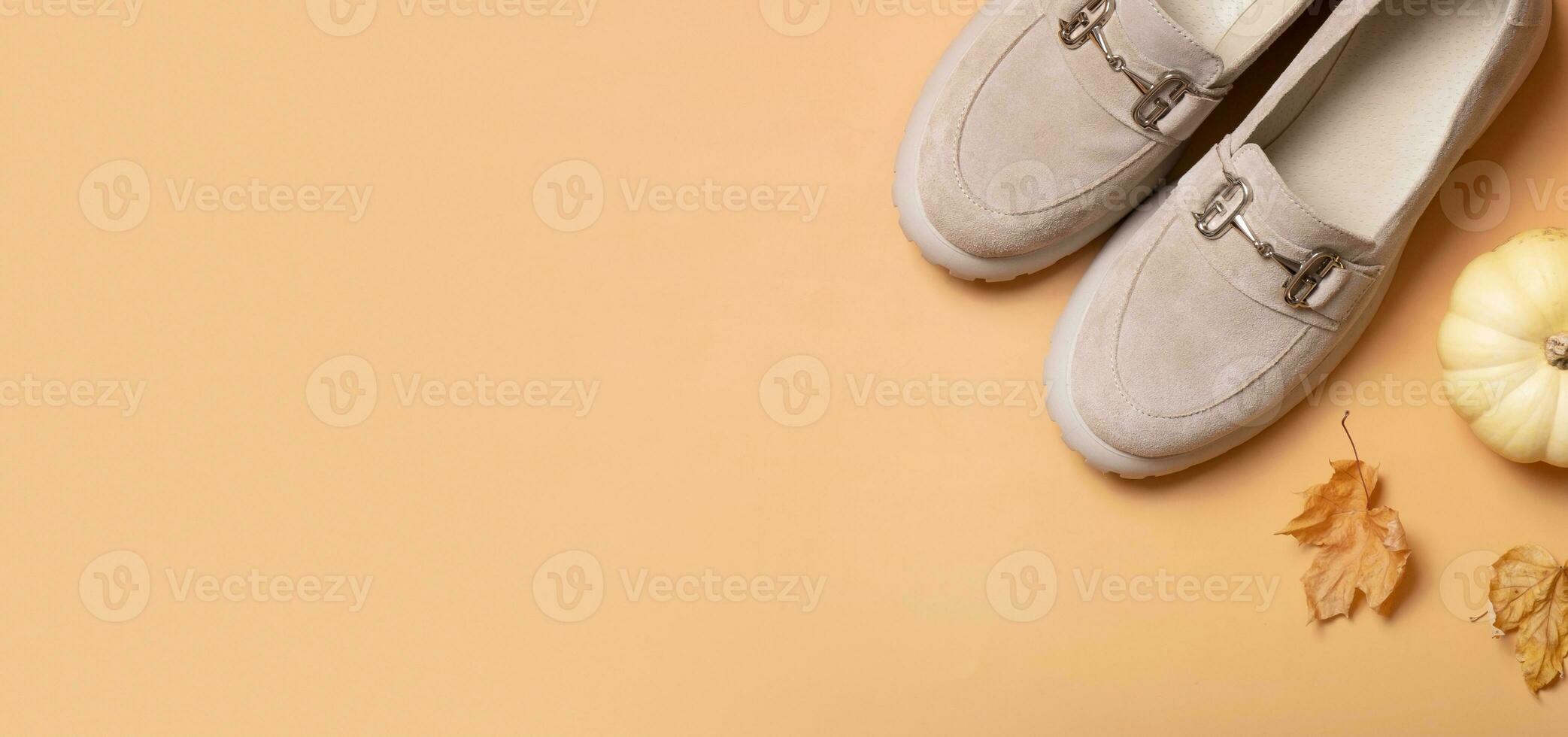 Banner with suede shoes with autumn leaves and pumpkin on orange background top view, flat lay photo