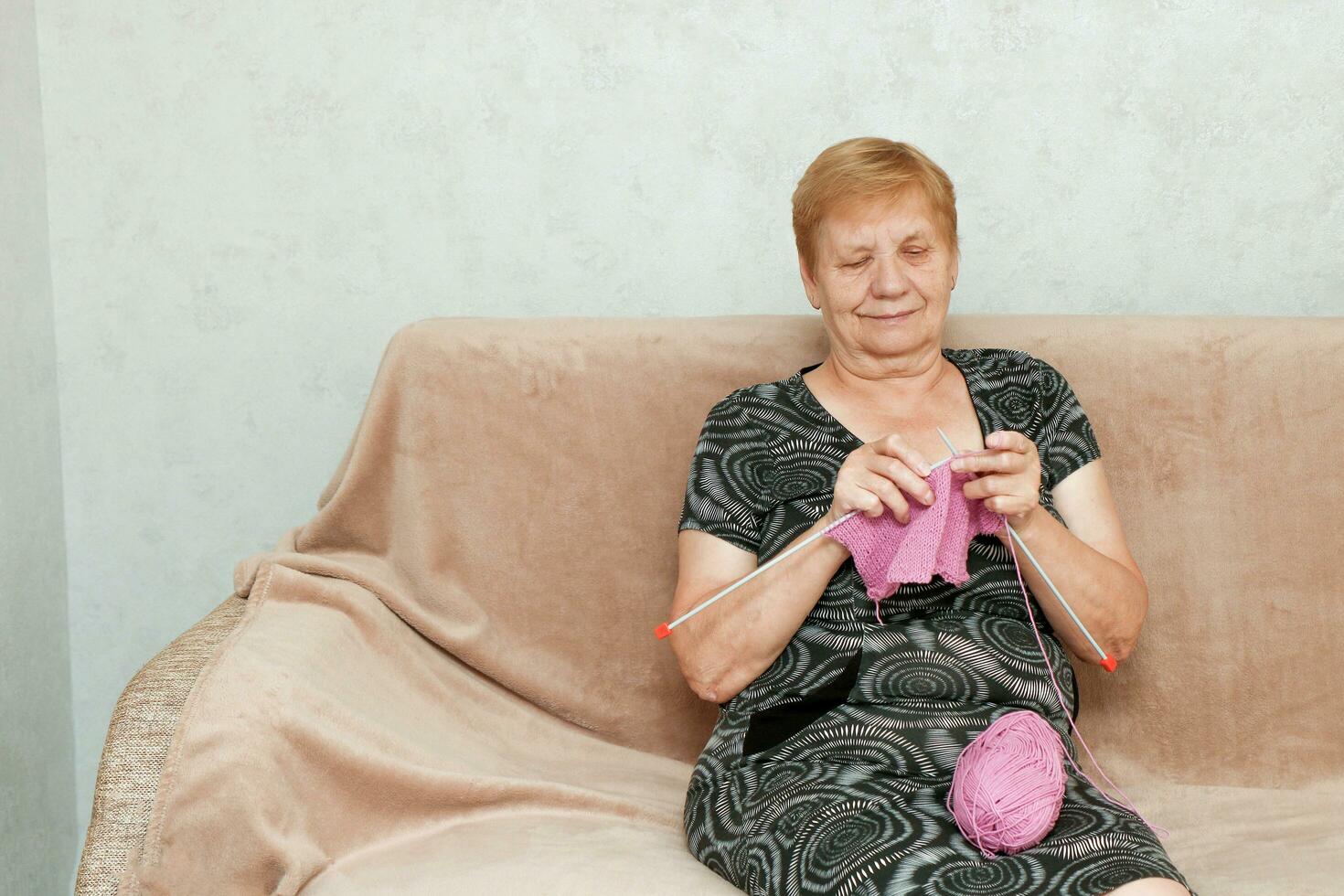 senior woman knitting sitting at home on the sofa photo