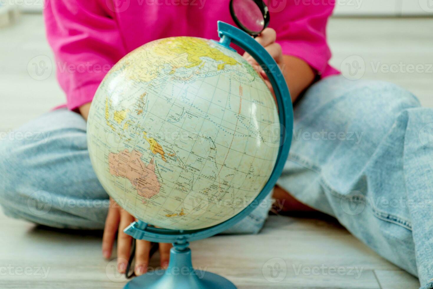 woman sitting on the floor looking at the globe through a magnifying glass photo