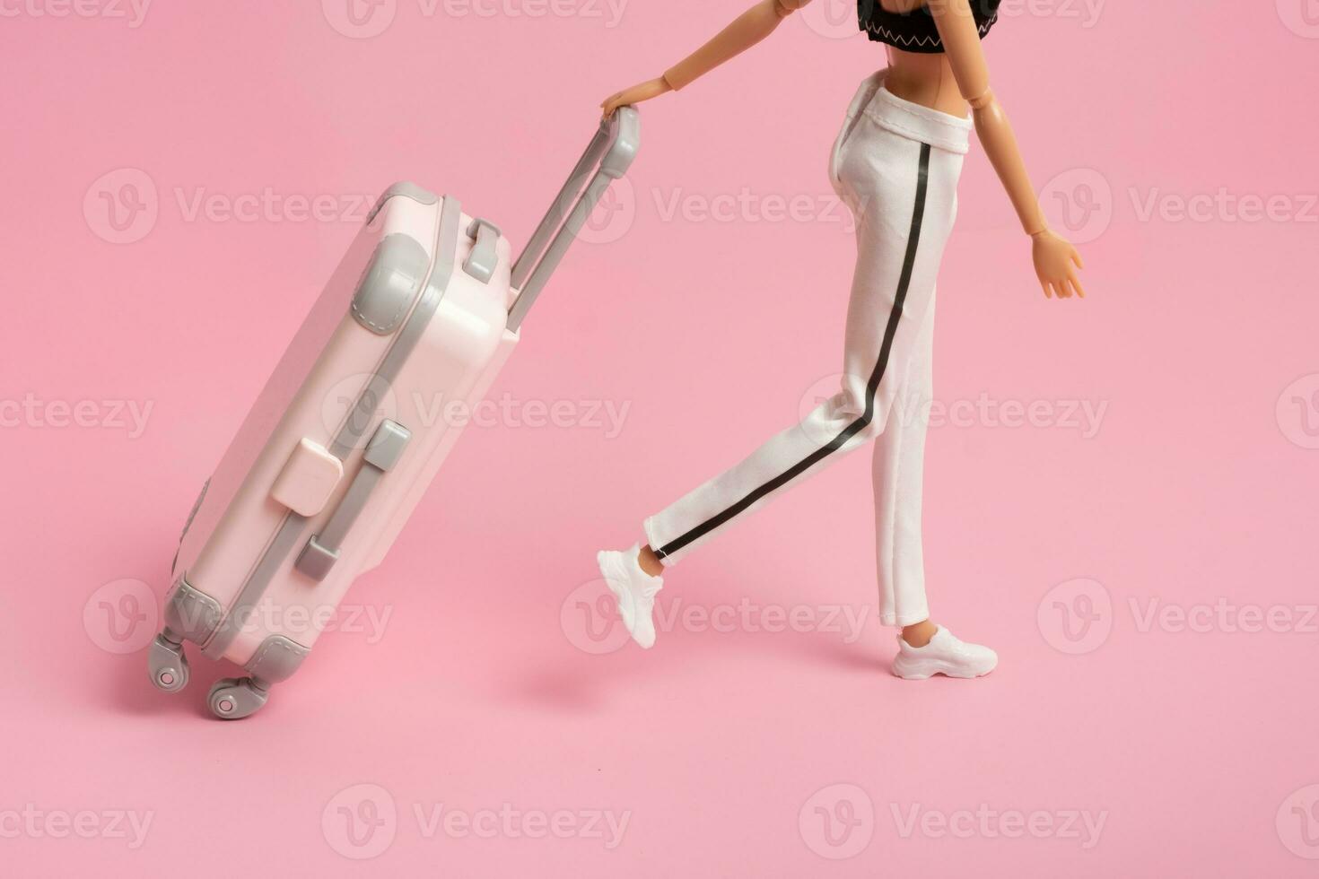 The doll carries a suitcase on wheels. Travel, vacation creative minimalistic concept photo