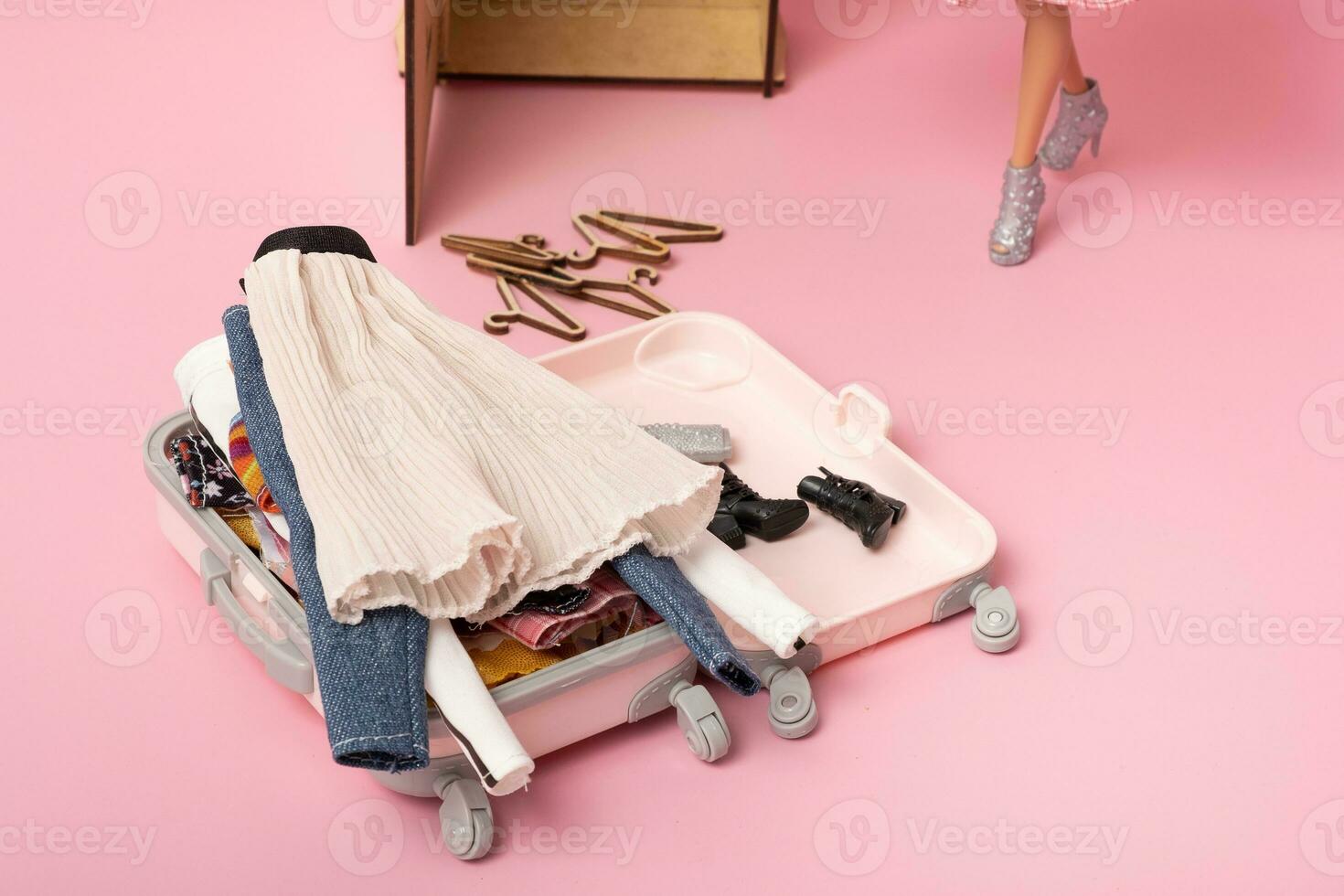 The doll puts clothes in a baggage. Preparing for traveling. Travel, vacation creative minimalistic concept. photo