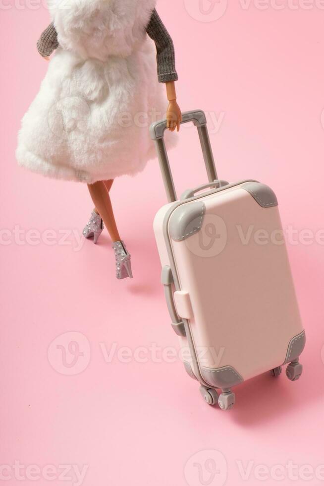 The doll carries a suitcase on wheels. Travel, vacation creative minimalistic concept photo